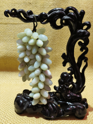 hand-carved mineral collectible titled Hanging Grapes of Abundance, featuring a cluster of grape-shaped stone beads suspended from a sculptural carved stand