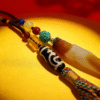 Detailed view of the Pangu inspired necklace highlighting layered agate pendant, Dzi bead, turquoise accent, and braided tassel on a golden surface