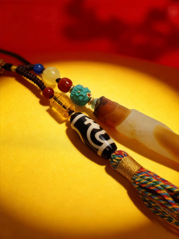 Detailed view of the Pangu inspired necklace highlighting layered agate pendant, Dzi bead, turquoise accent, and braided tassel on a golden surface