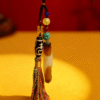 Close-up of the Primordial Layered Agate and Dzi pendant necklace showing turquoise bead, Dzi bead, amber tones, and hand-tied multicolor tassel