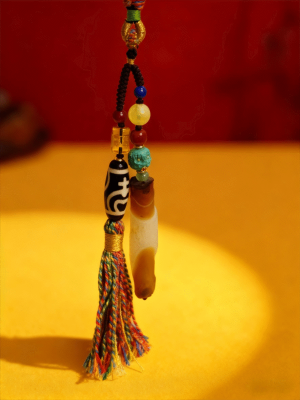 Close-up of the Primordial Layered Agate and Dzi pendant necklace showing turquoise bead, Dzi bead, amber tones, and hand-tied multicolor tassel