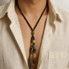 Model wearing the Primordial Layered Agate & Dzi pendant necklace, featuring layered agate, Dzi bead, and multicolor tassel on a black cord, styled with an open white shirt