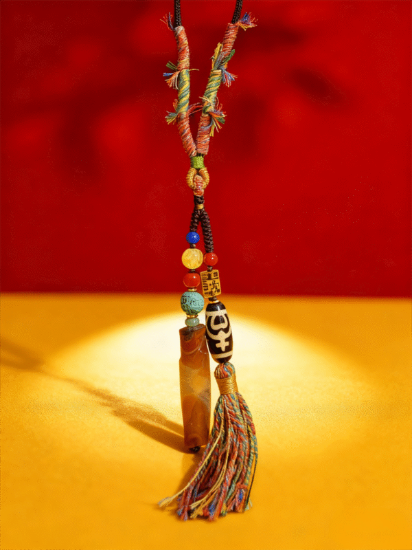 Pangu inspired necklace featuring a layered agate pendant and Dzi bead, suspended with multicolor tassel against a red and gold background symbolizing primordial creation