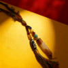 Artisan Pangu inspired pendant necklace with layered agate stone, Dzi bead, and colorful tassel photographed on red and gold background