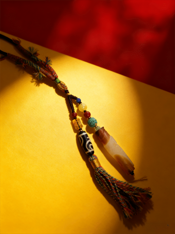 Artisan Pangu inspired pendant necklace with layered agate stone, Dzi bead, and colorful tassel photographed on red and gold background
