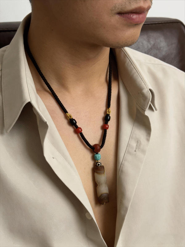 Primordial Layered Agate Pendant Necklace – Pangu Inspired Worn Look Male model wearing the Primordial Layered Agate Pendant Necklace, featuring a natural layered agate pendant with turquoise and red beads on a black hand-knotted cord, inspired by Pangu mythology