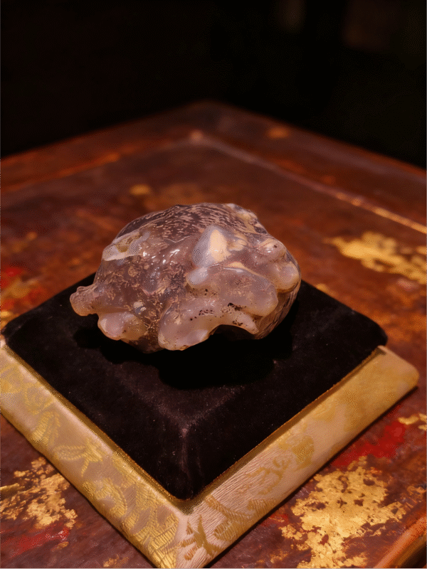 Stone Sentinel – Handheld Agate Artwork Handheld Agate Artwork titled Stone Sentinel, featuring a compact, guardian-like stone form displayed on a padded stand