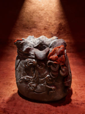 hand-carved mineral collectible titled The Treasure Pouch, featuring a sculptural agate vessel with intricate carved details and a pouch-like form displayed as a decorative object