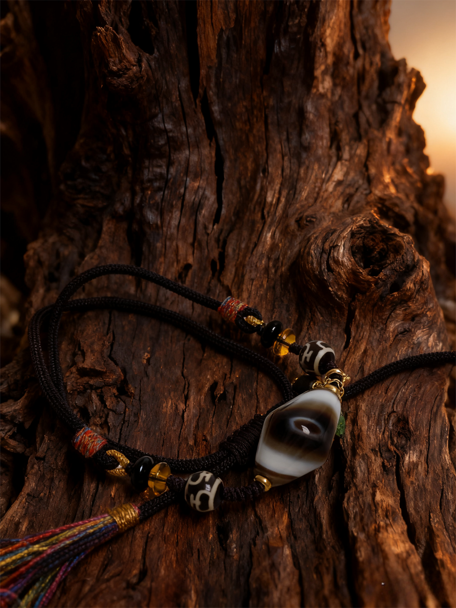 layered agate and dzi pendant necklace inspired by Gonggong, showcasing natural stone patterns, braided cord, and multicolor tassel on wood surface