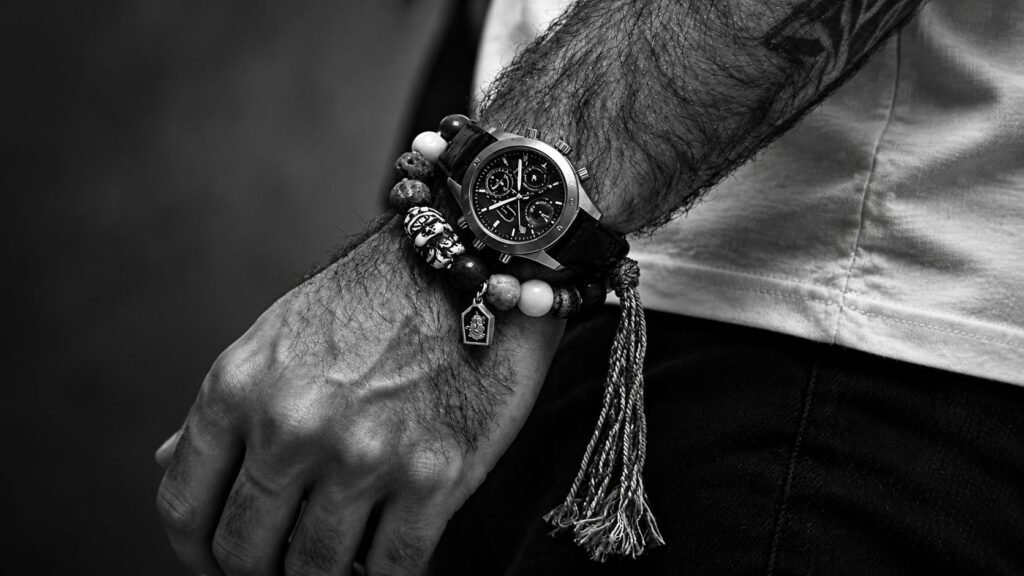 Man wearing a beaded gemstone bracelet with a wristwatch in a black-and-white styling photo.