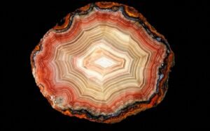 Close-up of a polished agate slice displaying intricate concentric bands in red, pink, cream, and white against a black background